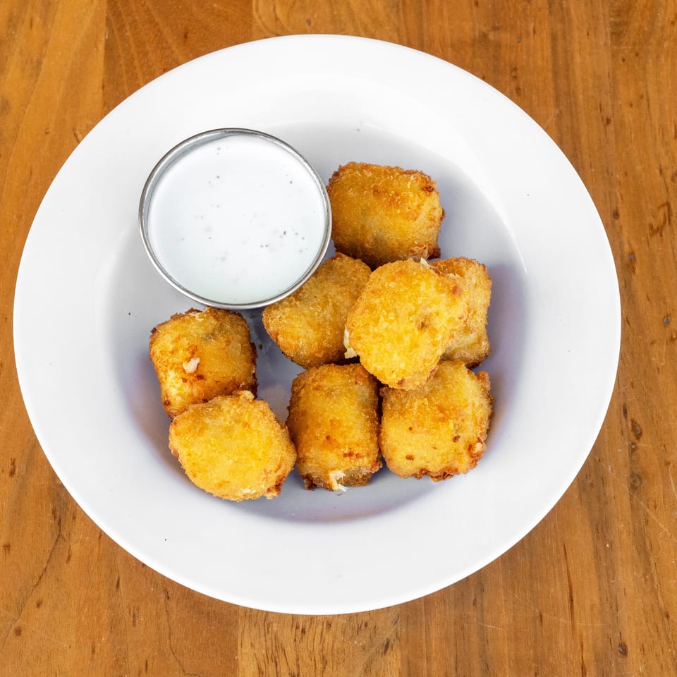 Golden fried bite-sized appetizers with creamy dipping sauce on a white plate over a wooden table.
