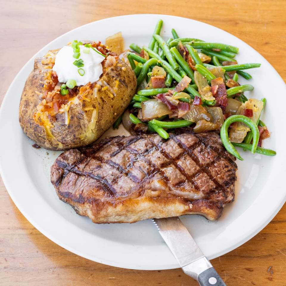 Grilled steak served with a loaded baked potato topped with sour cream and green onions, plus bacon-topped green beans.